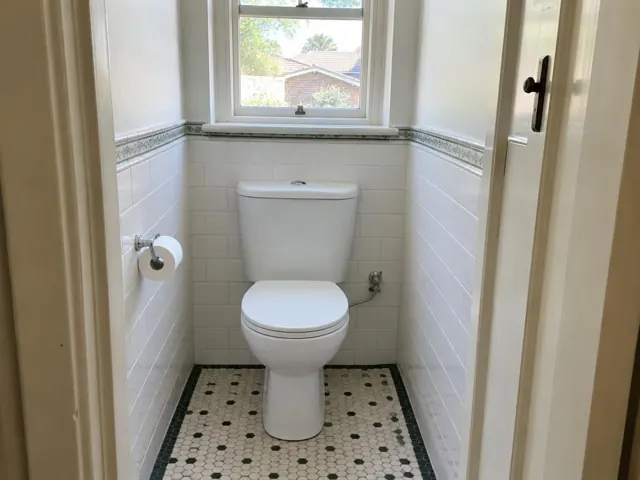 Clean white toilet in a tiled bathroom with a window and patterned floor in Freshwater