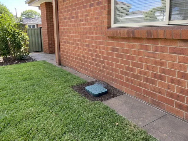 Capped sewer inspection opening beside a brick house wall and lawn in Manly Vale
